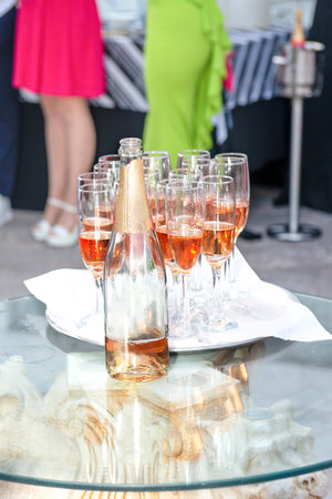 beautifully displayed glasses of sparkling wine and champagne with highlights on a tray at a festive event against the backdrop of dressed up peopleの写真素材