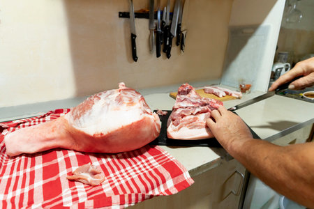 close-up hands of a man cutting raw pork meat with a knife on a board on the kitchen table.の写真素材