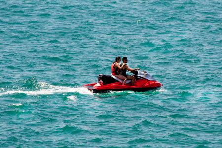 Two people in life jackets on a jet ski speeding through the ocean, creating a wake of splashes.Water transport, summer fun, water sportの写真素材