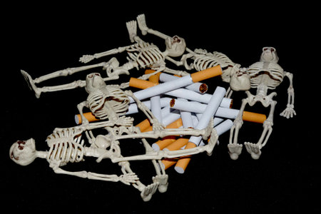 Several miniature skeletons lie around a stack of cigarettes on a black background. The concept of the danger and deadly consequences of smoking and tobacco addictionの写真素材