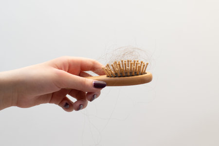 A beautifully manicured hand holds a wooden comb filled with tangled fallen hair, vitamin deficiency, stress, depression, breakage, thinning, healthの写真素材