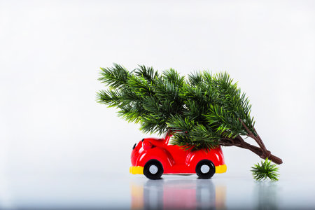 A toy car carries an evergreen tree on its roof a Christmas tree with a bow. Preparing for the Holiday, tree transportationの写真素材