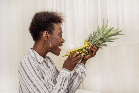 African black woman with short modern haircut demonstrates healthy lifestyle, holds ripe pineapple. Healthy habits, joy, positive, fruitarianismの写真素材