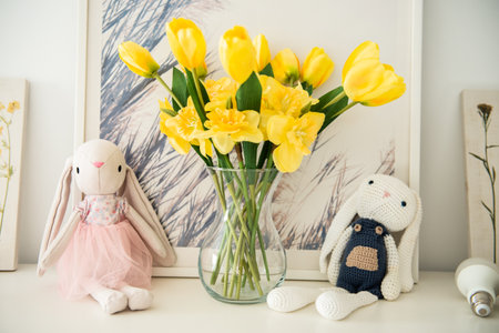 Plush bunnies next to a vase with yellow flower on a shelf decor for Easterの写真素材