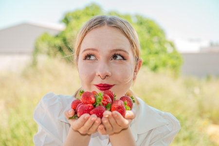 Young woman teenager smiling holding out fresh delicious strawberries, close-up, selective focus. Summer photo for social networks. Vitamin healthy snack.の写真素材