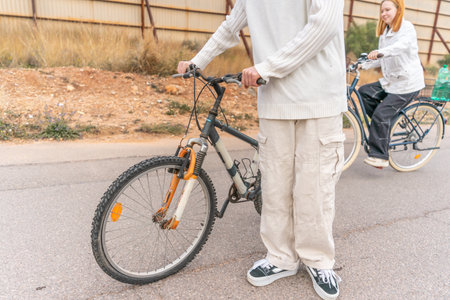 A young man pushes his bicycle CLOSE UP while a young woman rides behind him on the road.の写真素材