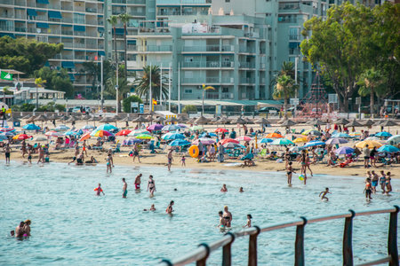 Many unrecognizable people swimming and sunbathing on a beach in the distance, colorful sun umbrellas, palm trees and hotels in the heatの写真素材