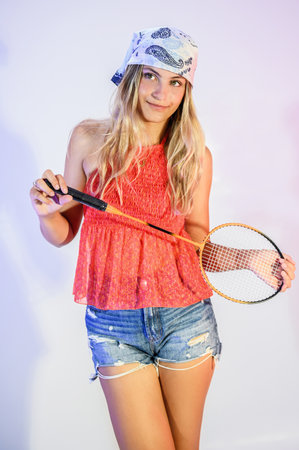A young woman in casual clothing holds a racket for badminton, posing. Youthful style. sports...