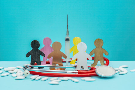 Colored figures stand around a syringe, medical instruments, and pills on a table. Vaccination and healthcare for different communities around the worldの写真素材