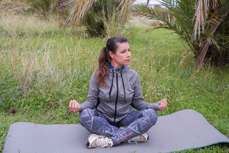 A woman doing morning energy exercises in the lotus position in a park. Doing yoga. Active recreation, meditation, and wellnessの写真素材