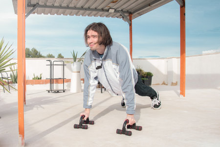 Man exercising on a rooftop using dip bars. Outdoor activity, home gym, calisthenics. Outdoor workout. Fitness, lifestyle, and wellnessの写真素材