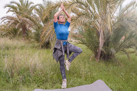 A woman practicing concentration and balance in a park with palm trees. Yoga. Outdoor activities.の写真素材