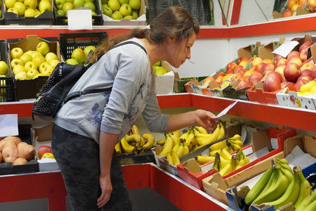 A woman looks at the price tag on fresh produce in the produce section of a supermarket, comparing prices and product selectionの写真素材