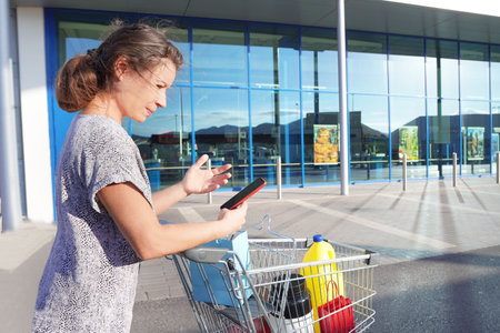 A woman with a shopping cart shares a sale on the phone against a supermarket backdropの写真素材