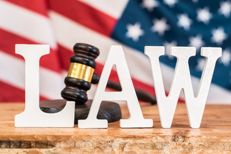 A gavel and the word LAW are depicted on a wooden surface in front of the United States flag. Symbolism of Justice and the American Legal Systemの写真素材