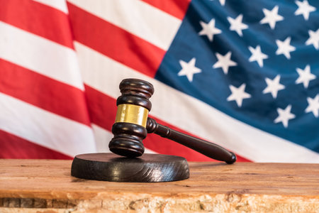 A judge's gavel on a wooden courtroom table in front of the United States flag. Symbolism of Justice and the American Legal Systemの写真素材
