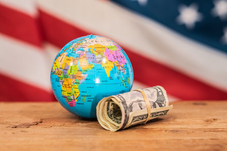Globe, roll of dollar bills on a wooden table with the United States flag. Importance of the...