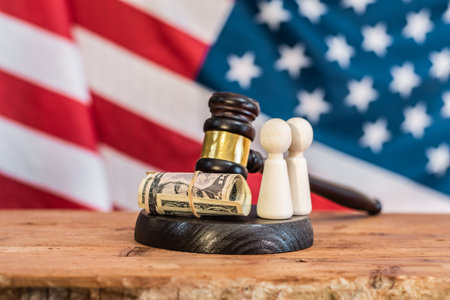 Judge's gavel, rolled-up money, and two figures against the backdrop of the American flag. Legal...