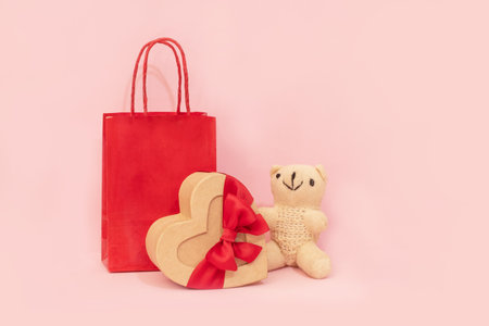 Romantic valentine gift set with a teddy bear, heart-shaped box, and gift bags on a pink background, holiday background.の写真素材