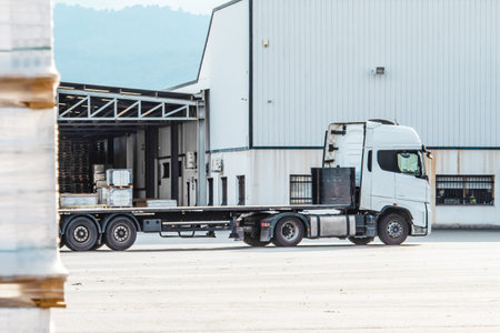 A flatbed truck in an industrial warehouse against a background of stacked pallets of...