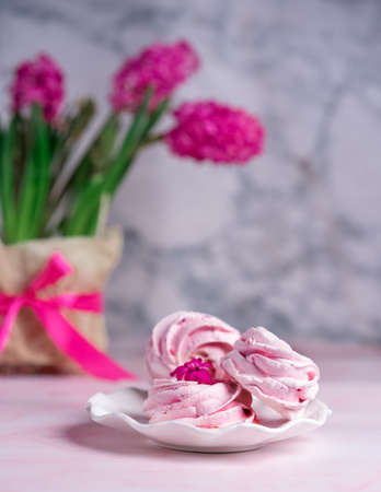 sweet pink marshmallows on a plate with a vase of spring flowers on the table against the background of gray marble. Morning coffee, breakfast, spring moodの写真素材