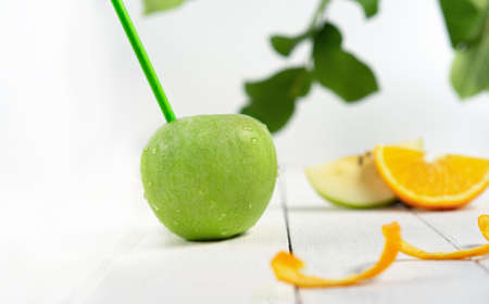 Sliced green apples with straws for juice with leavs and fruit slices on white wooden background, consept freshness and vitamins. Front view.の写真素材