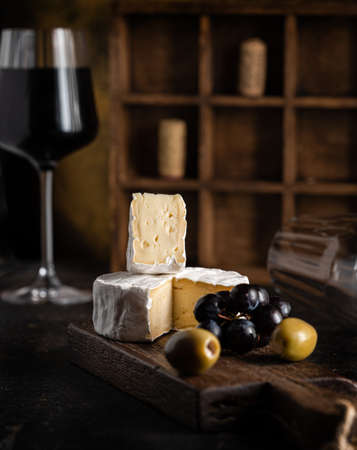 wine appetizer: cheese, olives and grapes are on the table next to a glass of red wineの写真素材