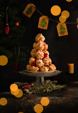 a postcard for the new year, profiteroles cakes are stacked on a hill, against the background of a Christmas tree and bokehの写真素材