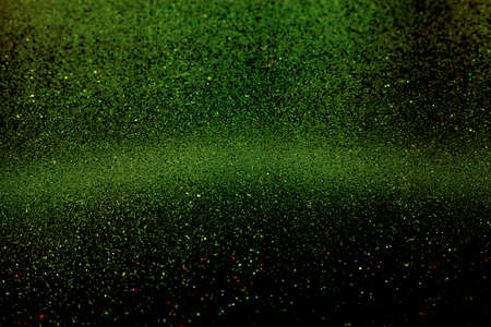 Abstract dark green defocused glitter holiday background. Falling stars. Selective focus of green sparkle with gradient, bright tone in the center. Design element for Christmas and New Year invitation. Concept of celebration and elegance.の写真素材