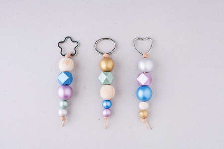 Keychains made of painted wooden beads with heart, star and oval shaped rings on a light background. Wooden beads and hexagon in pink, green, blue and gold metallic colors. Crafts and handmade concept.の写真素材