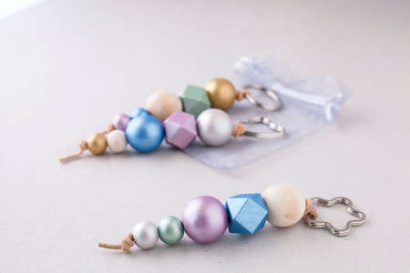 Selective approach of painted wooden bead key chains for car or bag on light background. Wooden beads and hexagon in pink, green, blue and gold metallic colors. Crafts concept.の写真素材