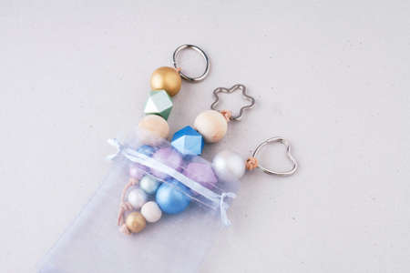 Painted wooden beads key chains in organza gift bag on light background. Wooden beads and hexagon in pink, green, blue and gold metallic colors. Top view, horizontal. Crafts concept.の写真素材