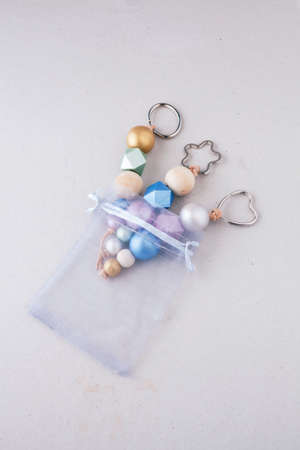 Painted wooden beads key chains in organza gift bag on light background. Wooden beads and hexagon in pink, green, blue and gold metallic colors. Top view, vertical. Crafts concept.の写真素材