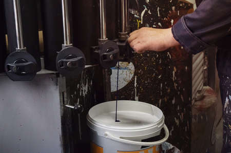 Production of paints. A worker in a suit with traces of paint stands near a paint can. Storage room for paints.の写真素材