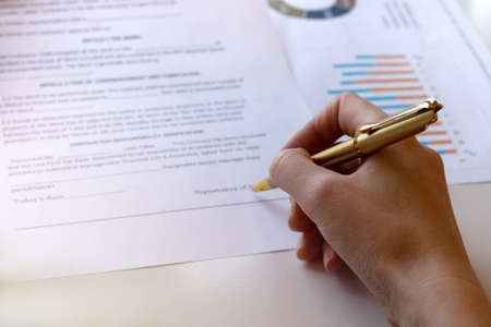 Young business woman signs a business contract on the background of economic charts while sitting at...