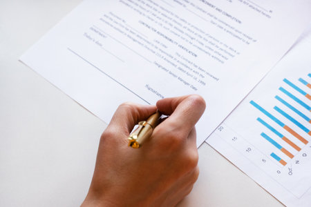 Young business woman signs a business contract on the background of economic charts while sitting at the table. Business and finance concept. Selective focus.の写真素材