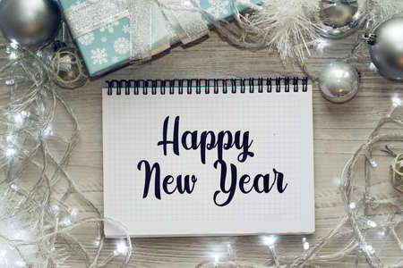 Notepad on the table with the text HAPPY NEW YEAR. Christmas background with decorations from balls and garlands. Delicate shades. Christmas or festive concept.の写真素材