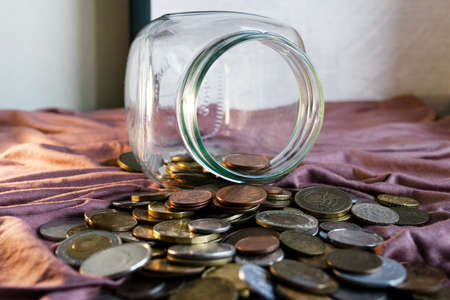 Scattered scattered coins on the table along with a glass jar. The concept of finance, economy.の写真素材