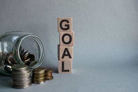 The inscription GOAL on wooden cubes isolated on a light background along with a glass jar with coins, business and finance concept.の写真素材