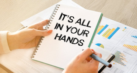 A business woman sitting at a table in a light office holds a notebook with notes in her hands, against the background of business charts and business documents. Close-up, soft light.の写真素材