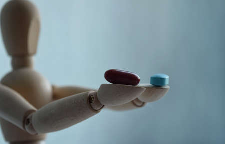 Wooden figurine of a man, holding two pills, on a light background with free space for your text. Medicine and healthcare concept.の写真素材