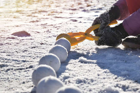 A child makes snowballs out of snow using a snowball toy. Winter frosty sunny day in nature. Winter children's outdoor games.の写真素材