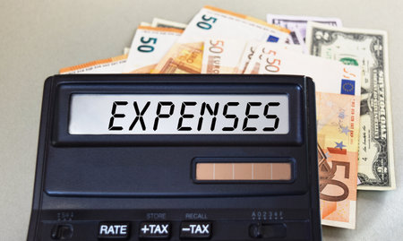 EXPENSES text written on a calculator next to the background of euro banknotes. finance or business...