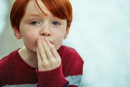 6 year old redheaded boy with his hand to his mouth to blow a kissの写真素材