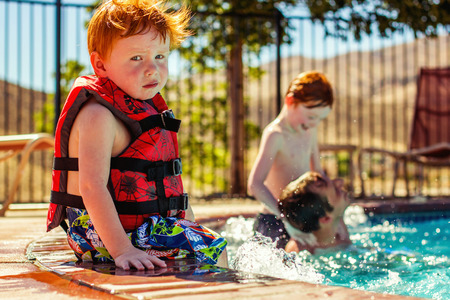 2 year old boy sitting on the edge of the pool with life jacketの写真素材