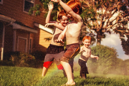 three redhead brothers playing in the sprinklers on a hot summer dayの写真素材