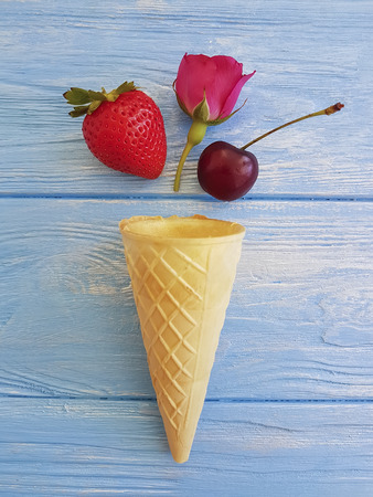 cone for ice cream, strawberry, cherry rose flower pattern on a blue wooden backgroundの写真素材
