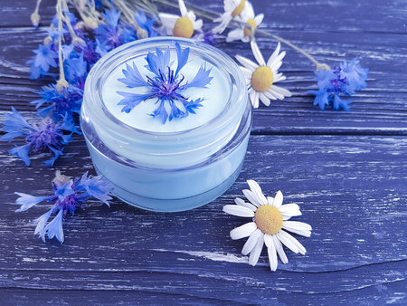 cream cosmetic flowers cornflower, camomile on a dark wooden backgroundの写真素材