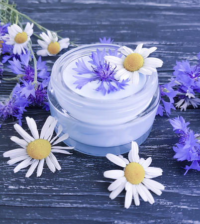 cream cosmetic flowers cornflower, camomile on a dark wooden backgroundの写真素材