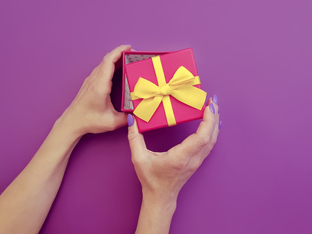 female hands manicure, gift box on a colored background paper